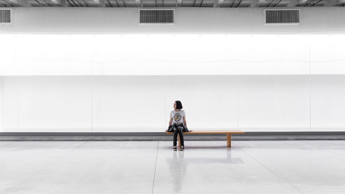 Una mujer sentada en un banco en una habitación grande sin muebles, Guilherme Stecanella, unsplash.com